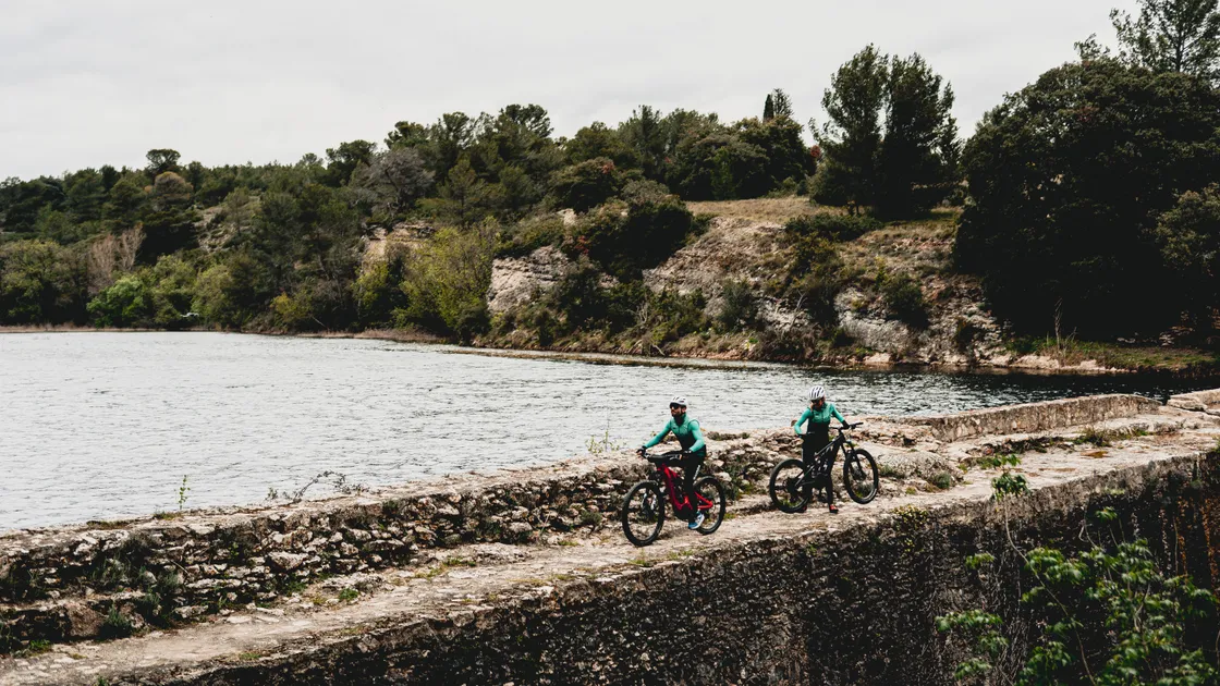Deux vététistes en VTT électrique sur un chemin offrant un point de vue sur un lac